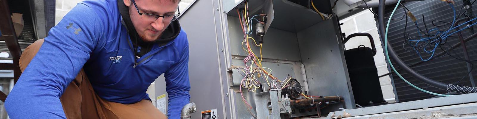 Student kneeling with wrench beside open AC unit