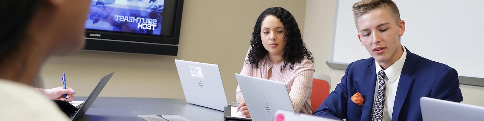 Students in business apparel working at a conference room table. Southeast Tech image displayed on screen.